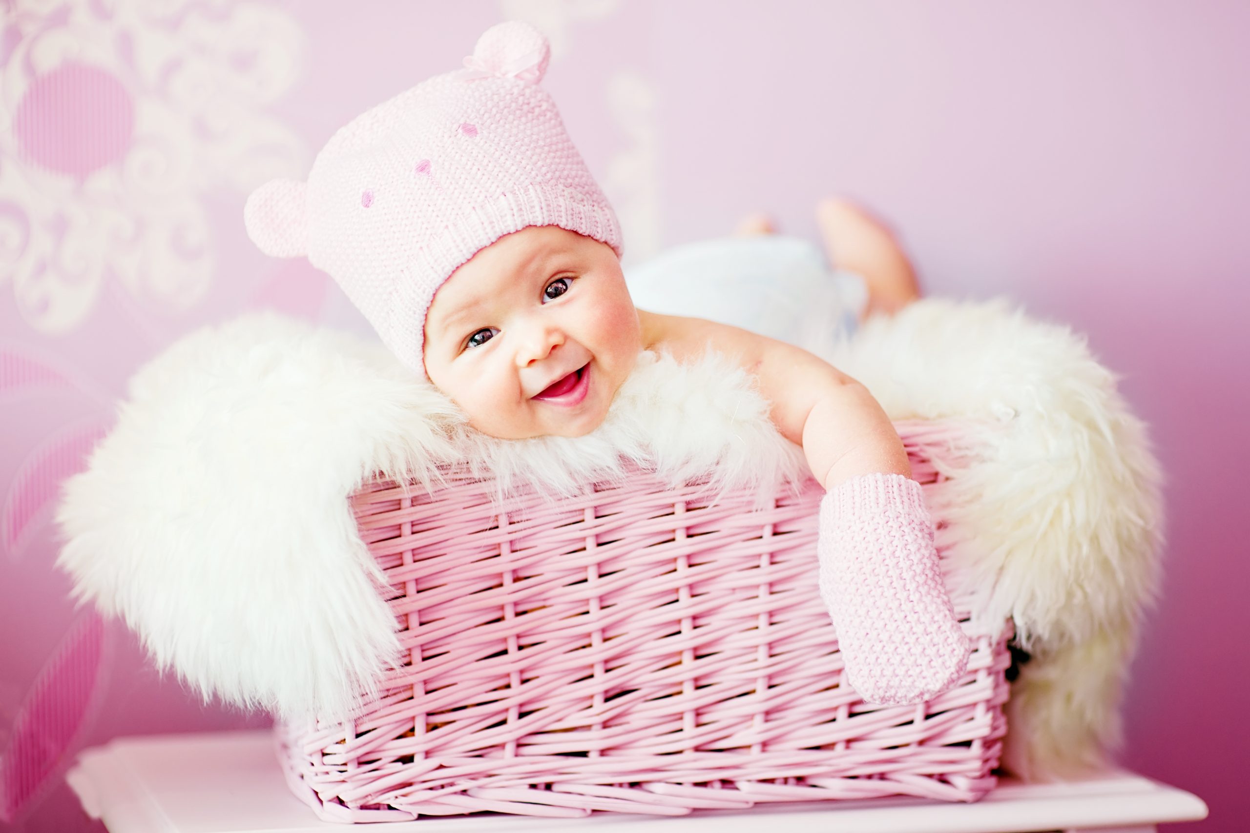 baby girl in pink knitted bear hat lies at basket